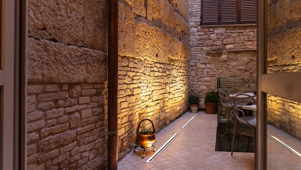 Un patio con paredes de piedra, un espacio de estar al aire libre de estilo rústico, una mesa de metal y una planta en maceta.