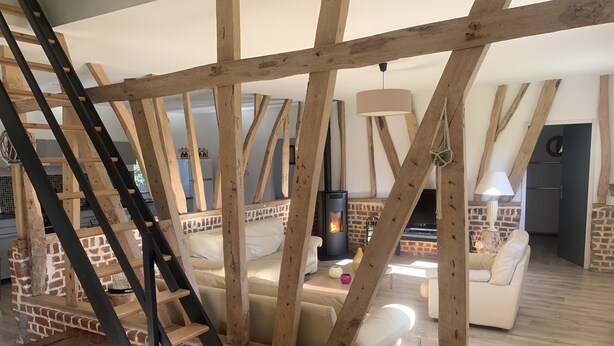 A rustic interior with exposed wooden beams, a fireplace, and a staircase leading to a loft area.