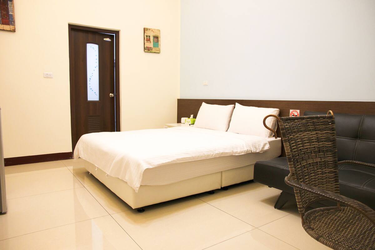 A hotel room with a bed, a chair, and a door.