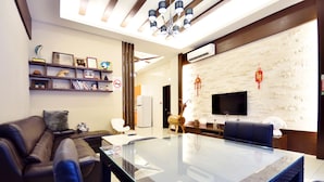 A modern living room with a glass-top table, leather sofa, and a flat-screen TV mounted on the wall. - Kai Feng B&B (Taitung)