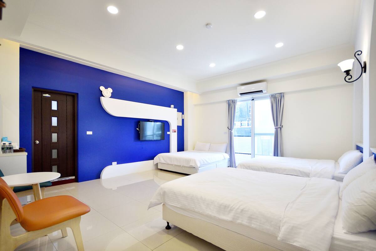 A hotel room with two beds, a TV mounted on the wall, a small table, and a chair.