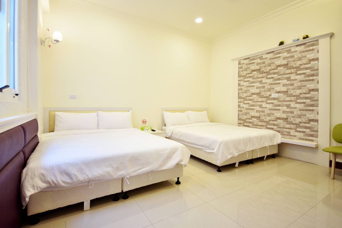 A room with two beds, a window, a wall-mounted shelf, and a chair.