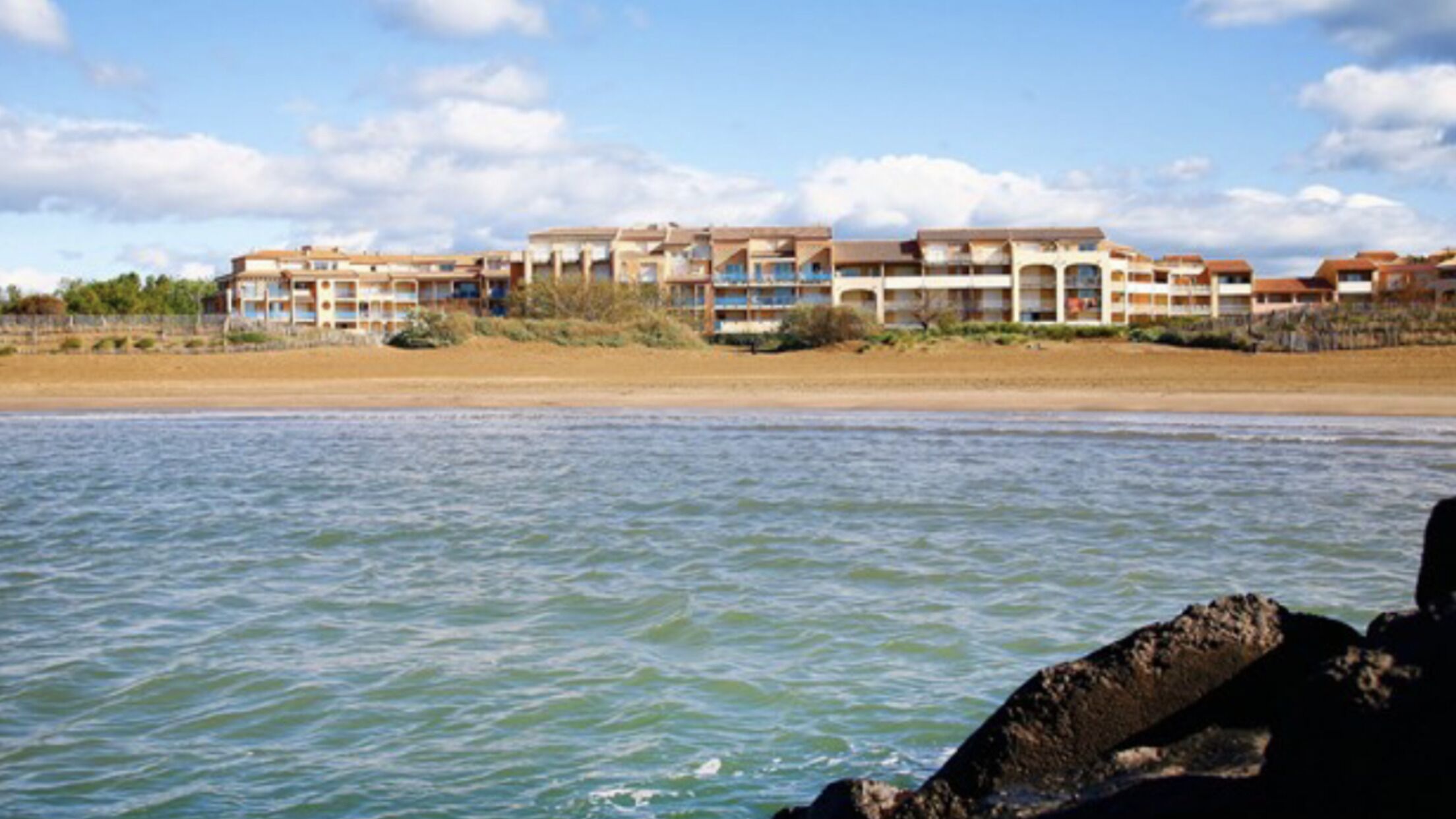 A beachfront hotel with multiple buildings, a sandy beach, and calm water.