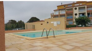 Una piscina con solárium empedrado, rodeada por un edificio con varios balcones y un techo plano.