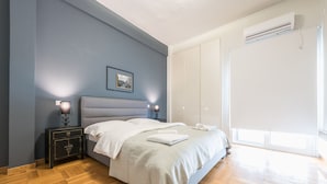 Un dormitorio con cama, mesitas de noche, un cuadro enmarco y un equipo de aire acondicionado.