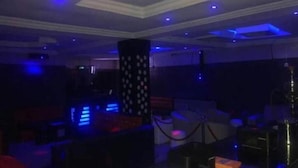 A dimly lit room with a bar area, a pillar with a pattern, and a table with a bottle and a box. - Galpin Suites Ikeja (Lagos)