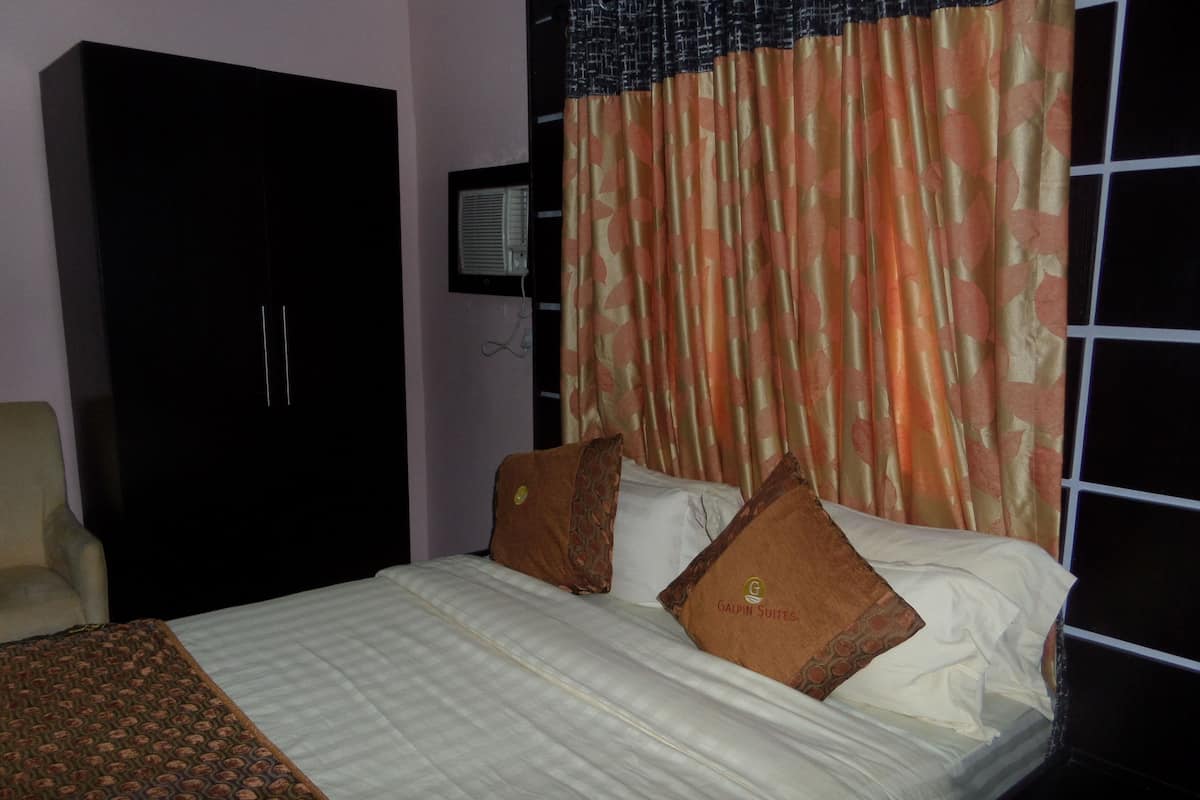 Quarto de hotel com cama, guarda-roupa, cadeira e janela com cortinas.