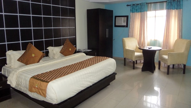 A hotel room with a large bed, two armchairs, a small table, a wardrobe, and a window with curtains. - Galpin Suites Ikeja (Lagos)