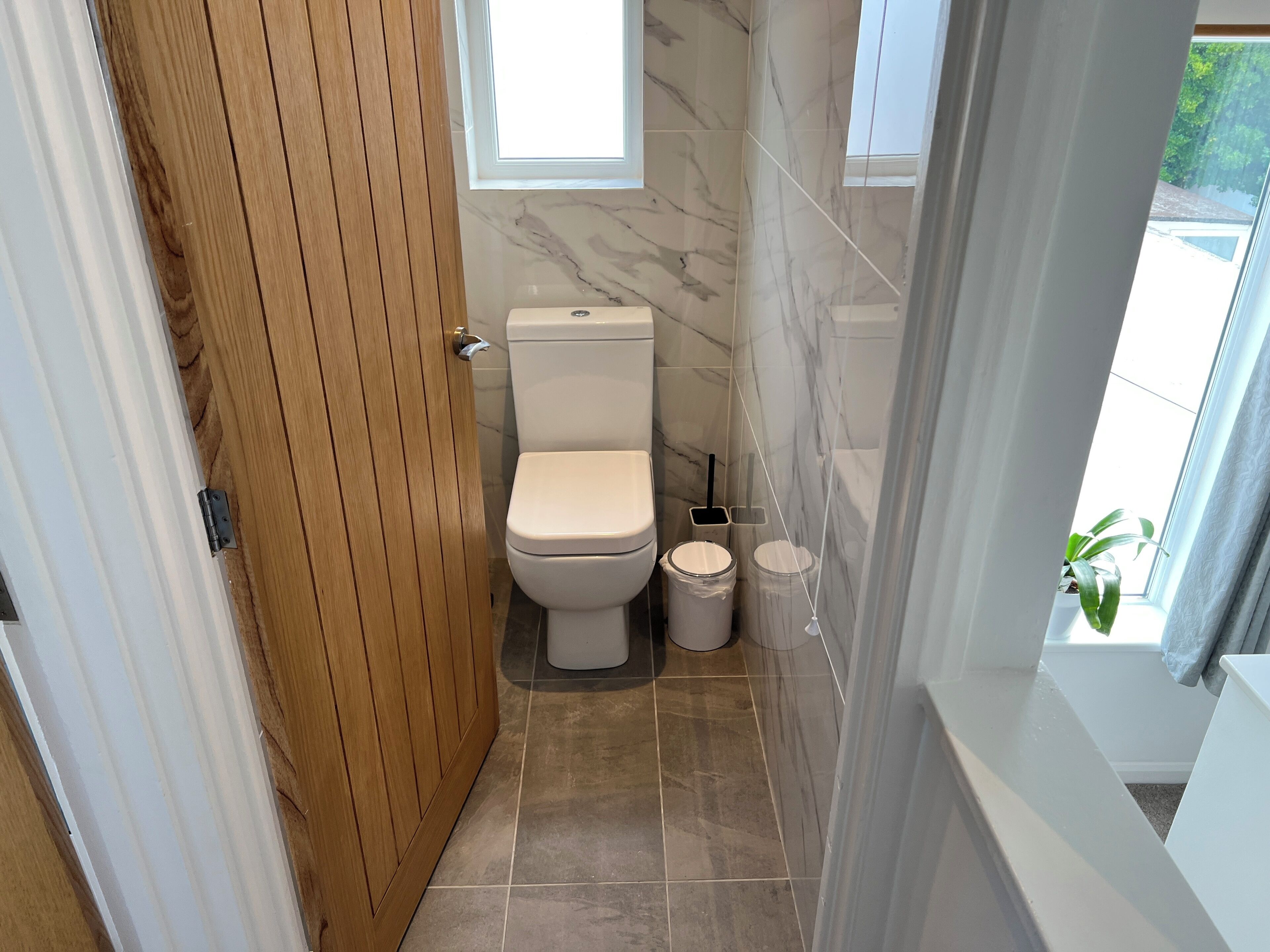 A bathroom with a toilet, marble walls, and a wooden door.