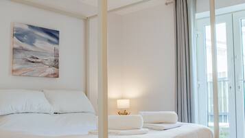 A four-poster bed with white bedding, a bedside lamp, and a painting on the wall.