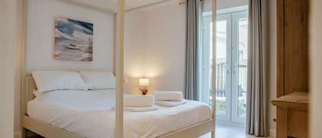 A four-poster bed with white linens, a bedside lamp, and a painting on the wall.