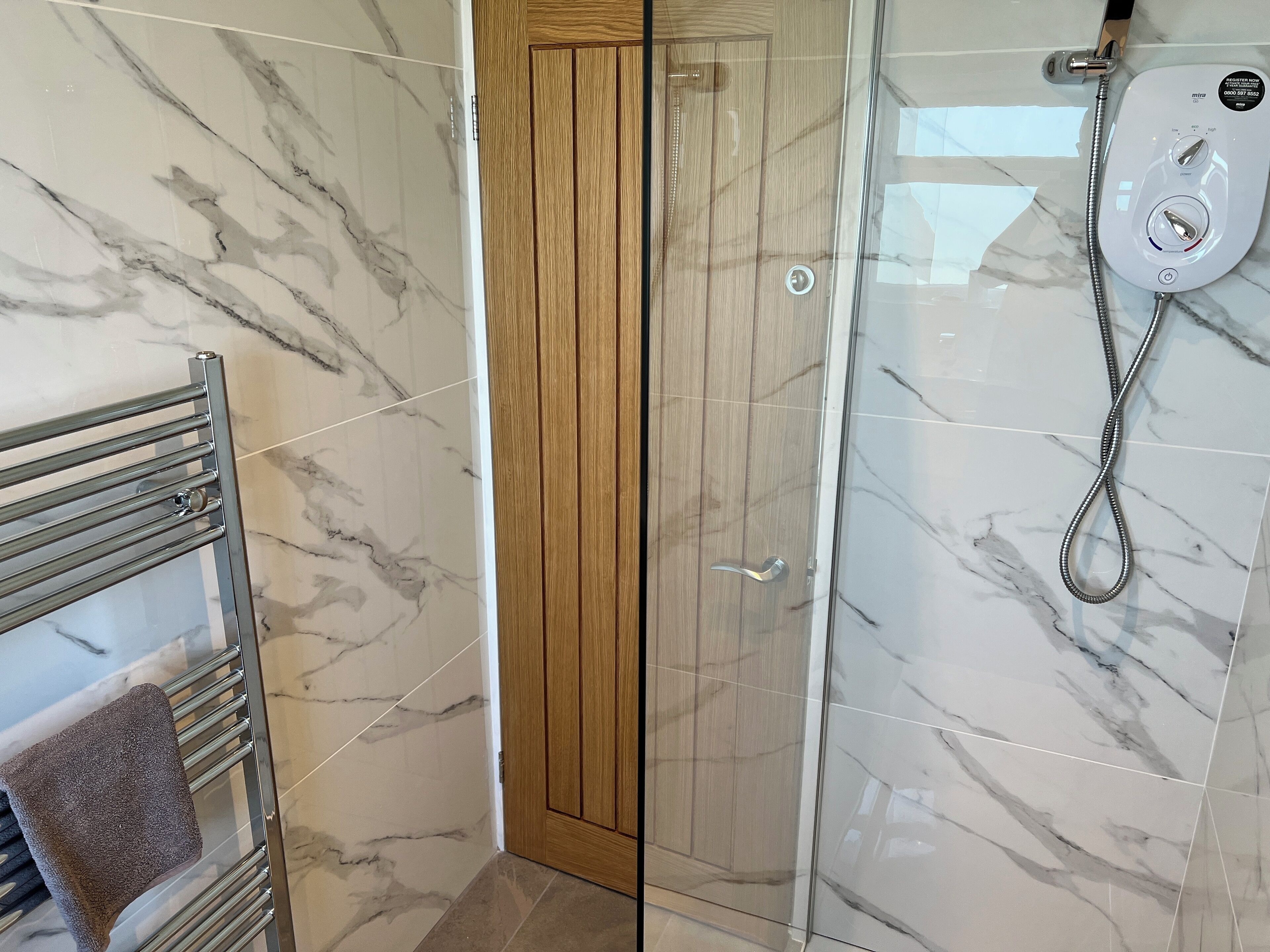 Un bagno con doccia vetrata, una porta in legno e un porta asciugamani con un asciugamano.