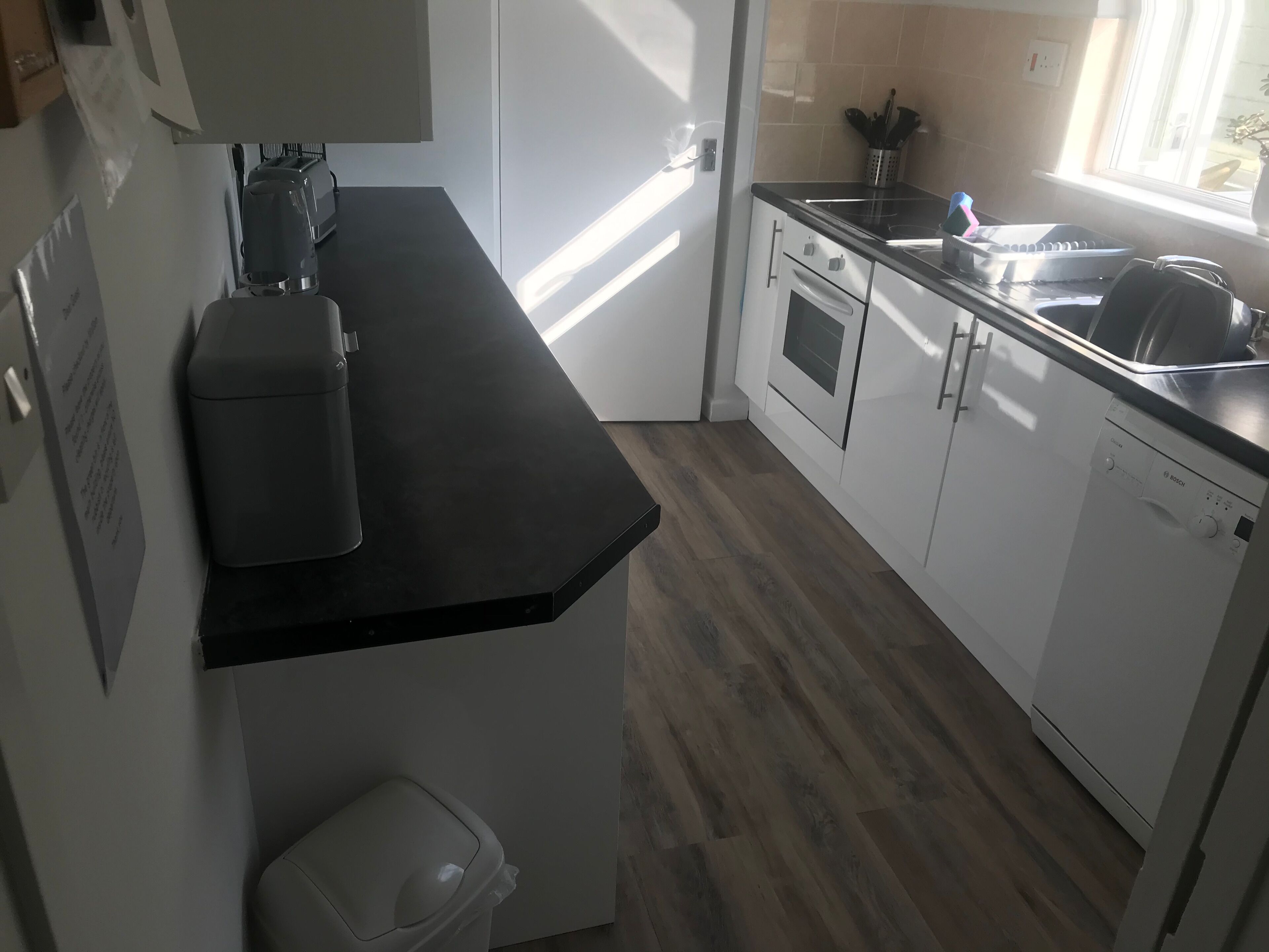 Une cuisine moderne avec des meubles blancs, un plan de travail noir et un lave-vaisselle Bosch.
