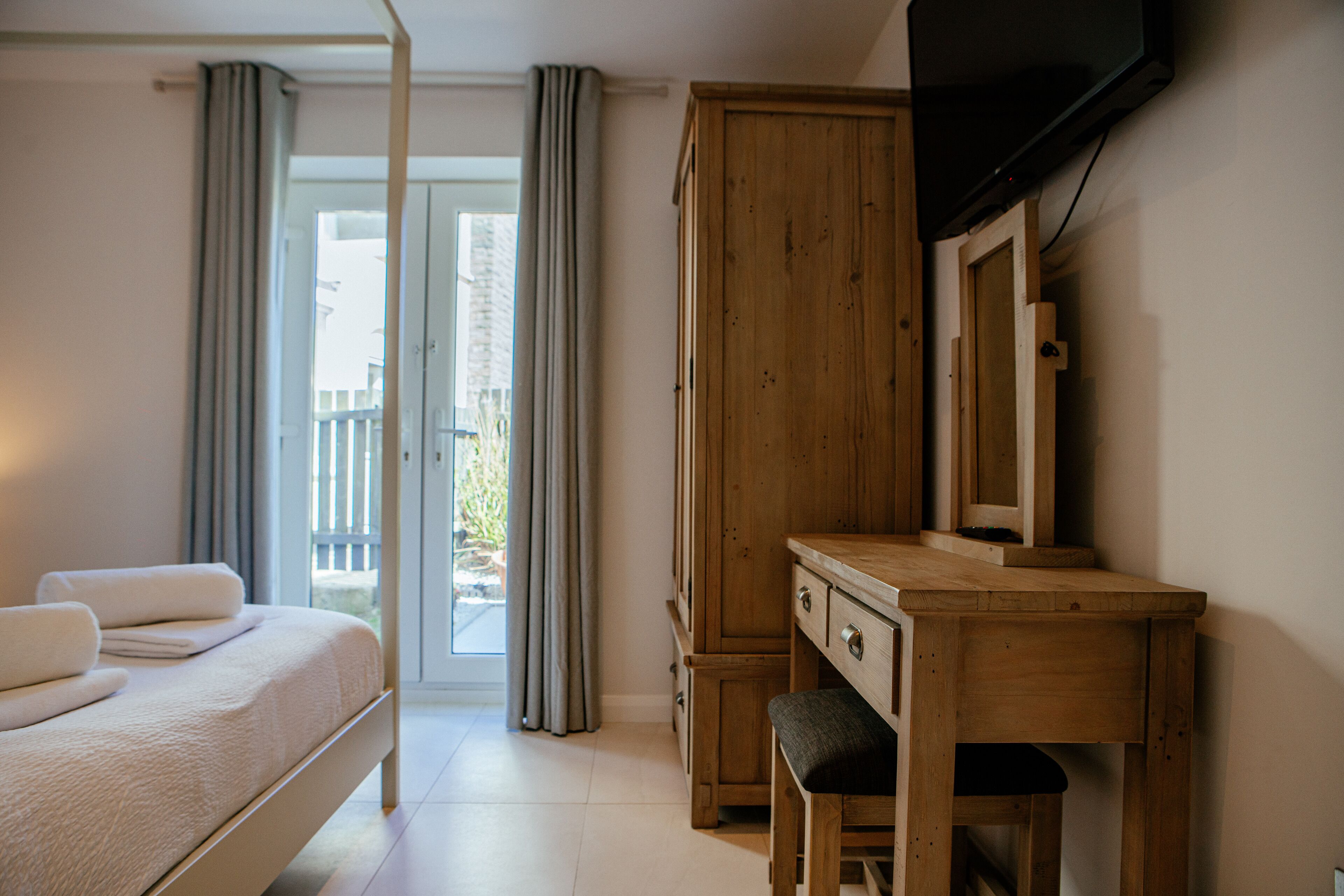 A bedroom with a bed, a wooden desk, a chair, a television, and a large wardrobe.