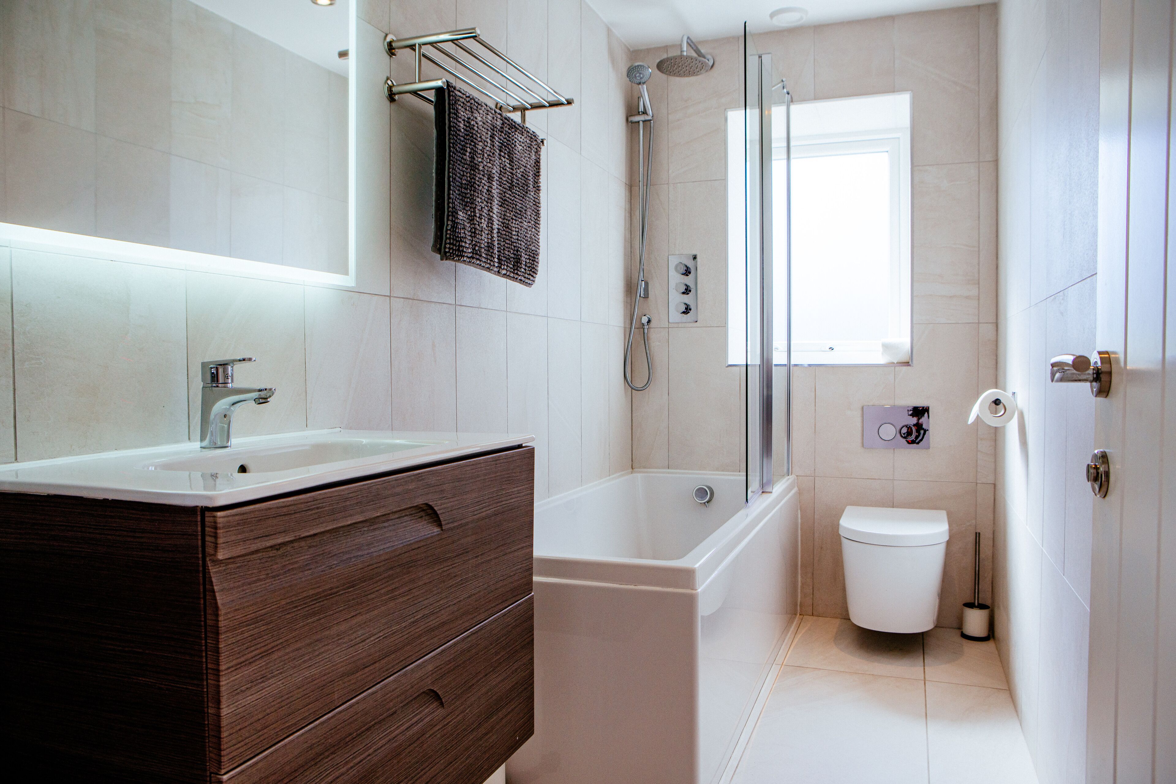 Et moderne badeværelse med et trækommode, badekar, toilet og brusekabine med glasvægge.