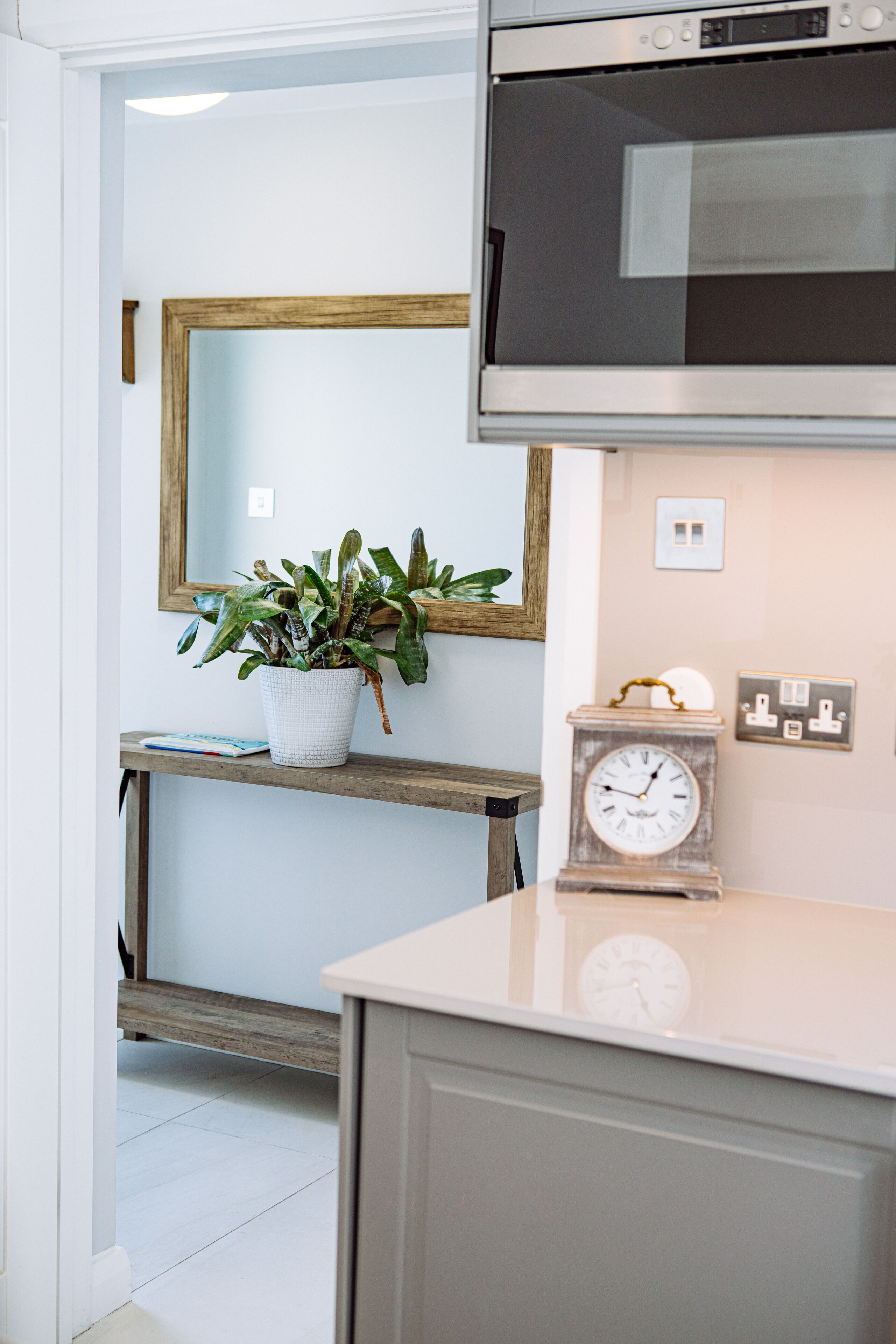 Una cocina con microondas, un reloj y una planta en maceta sobre una estantería.