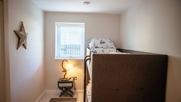 A small, neatly arranged bedroom with a bunk bed, a bedside lamp, a star decoration, and a window with blinds.