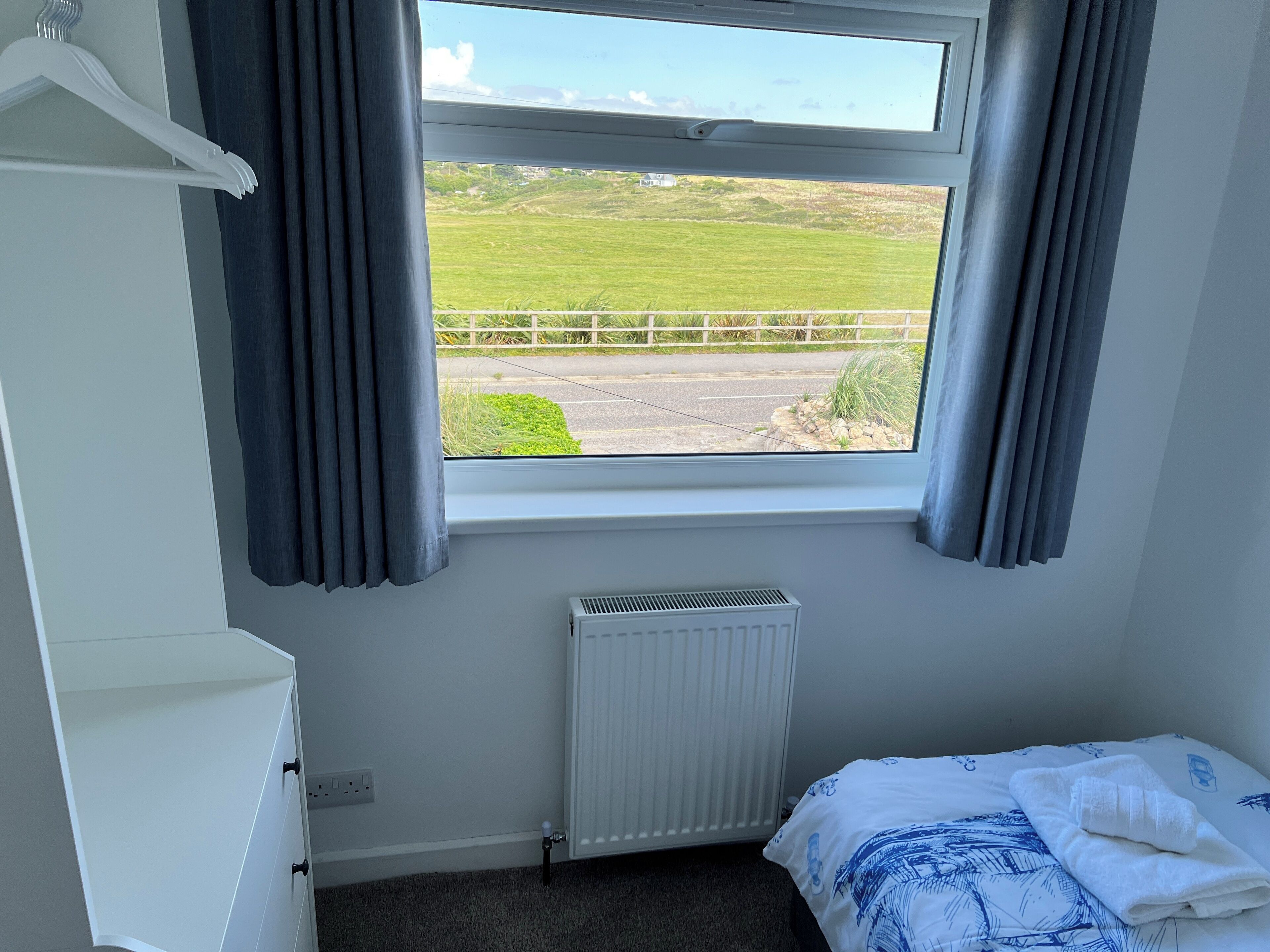 A bedroom with a window view of a green field and a road.
