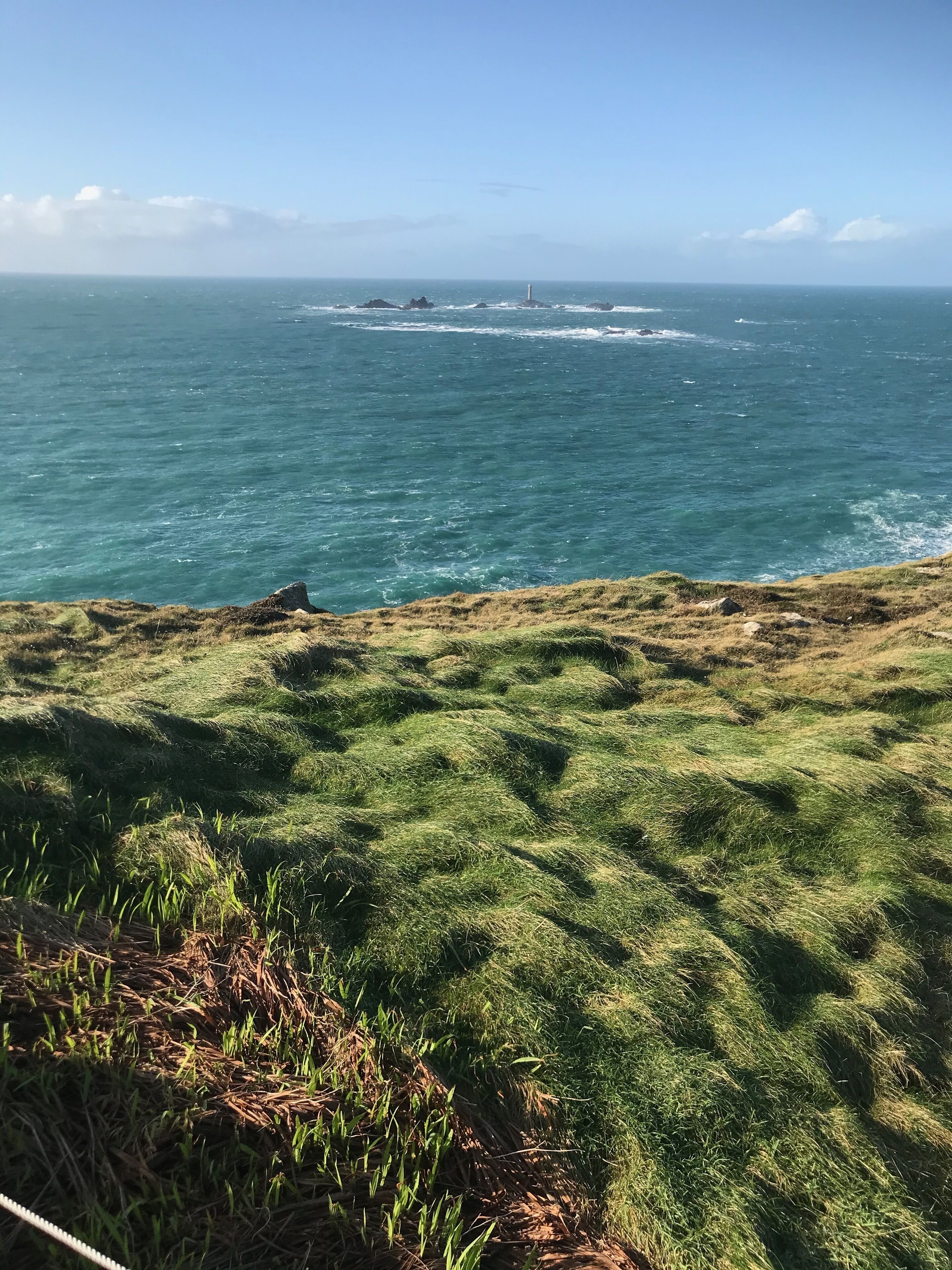 A grassy coastal landscape with a lighthouse in the distance.