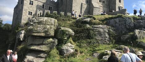 A historic stone castle with a large tower, situated on a grassy hill with visitors around.