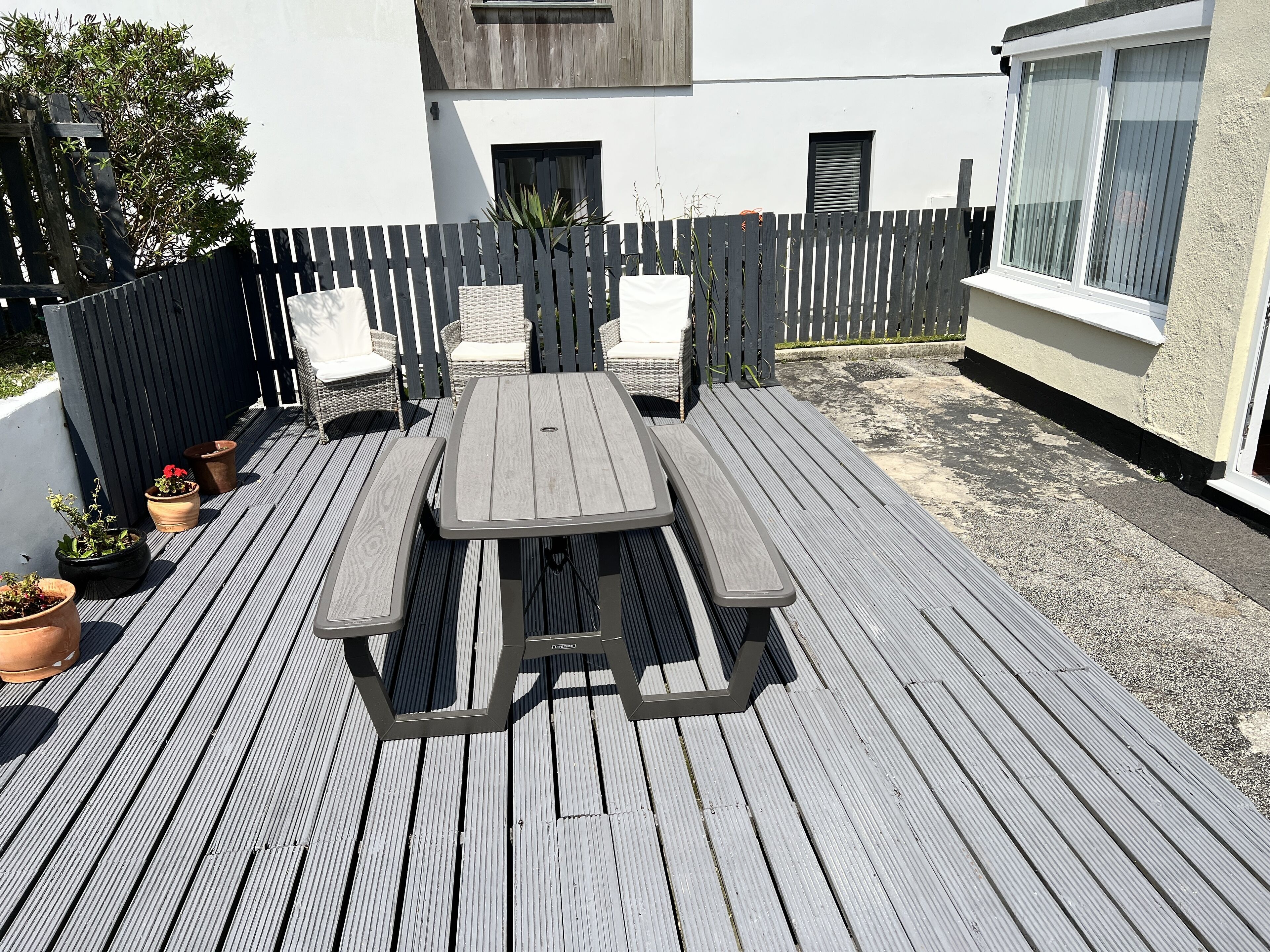 A wooden deck with a picnic table and chairs, surrounded by a fence and potted plants.