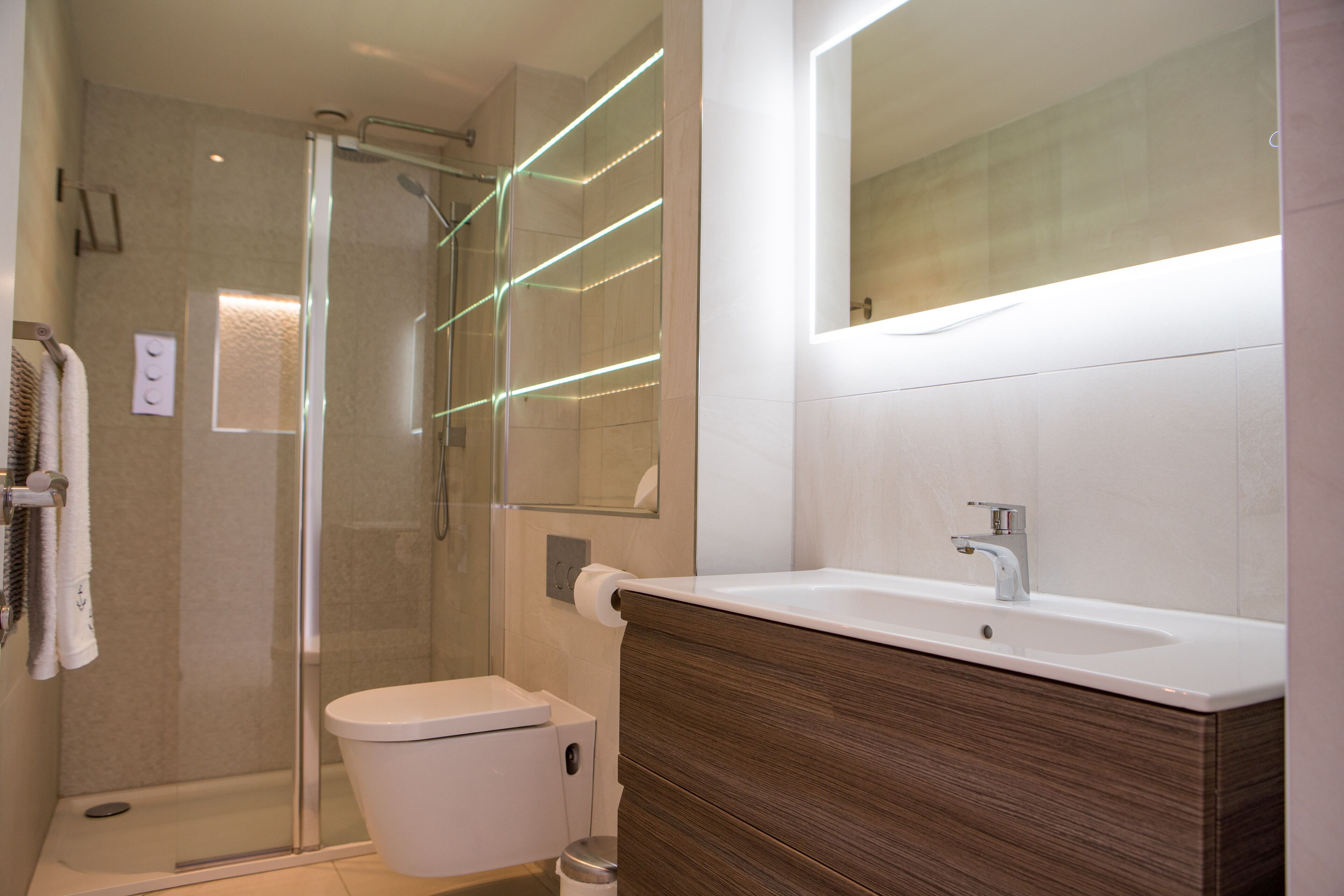 A modern bathroom with a glass-enclosed shower, a white toilet, a wooden vanity, and a large mirror.