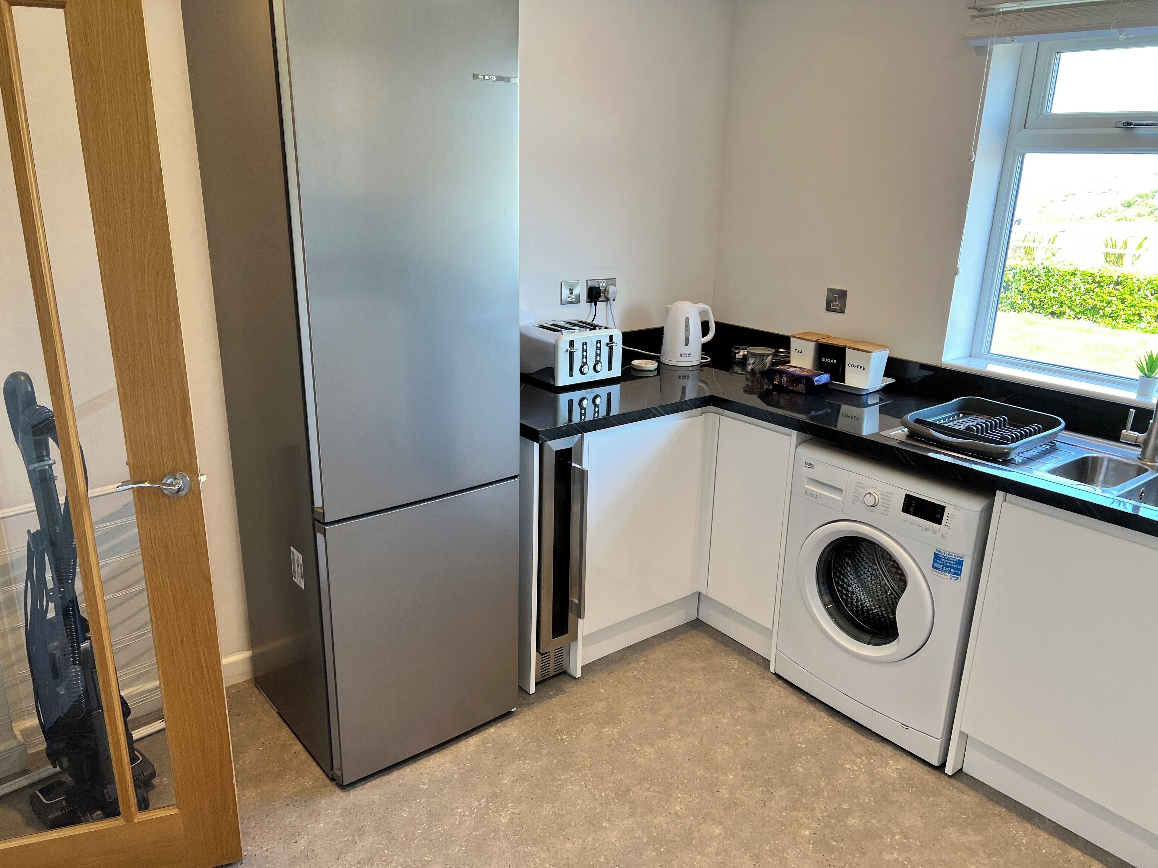 Eine kompakte Küche mit Edelstahlkühlschrank, Waschmaschine, Kaffeemaschine und Toaster.