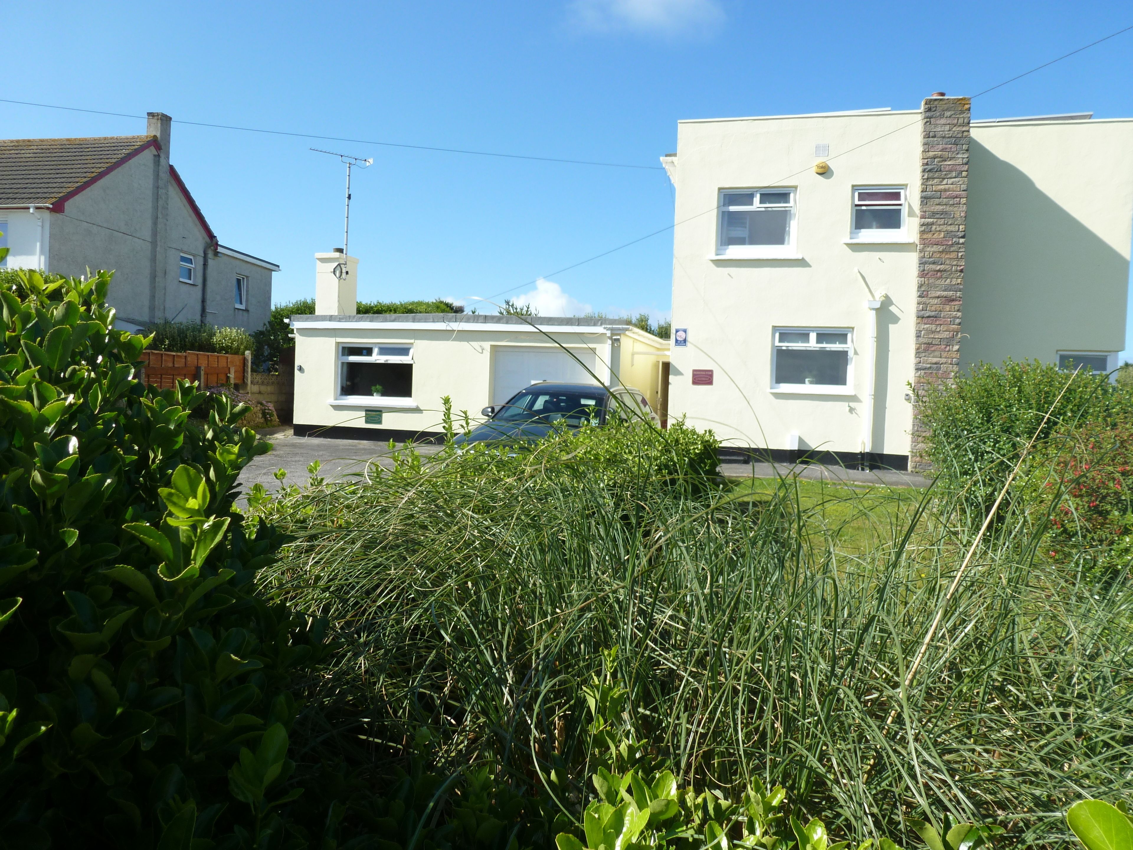 A two-story residential building with a garage, surrounded by greenery and a parked car.