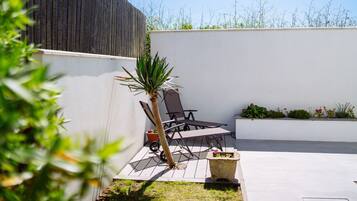 Un espace patio aménagé avec une table et des chaises, un petit palmier et un jardinier avec des fleurs.