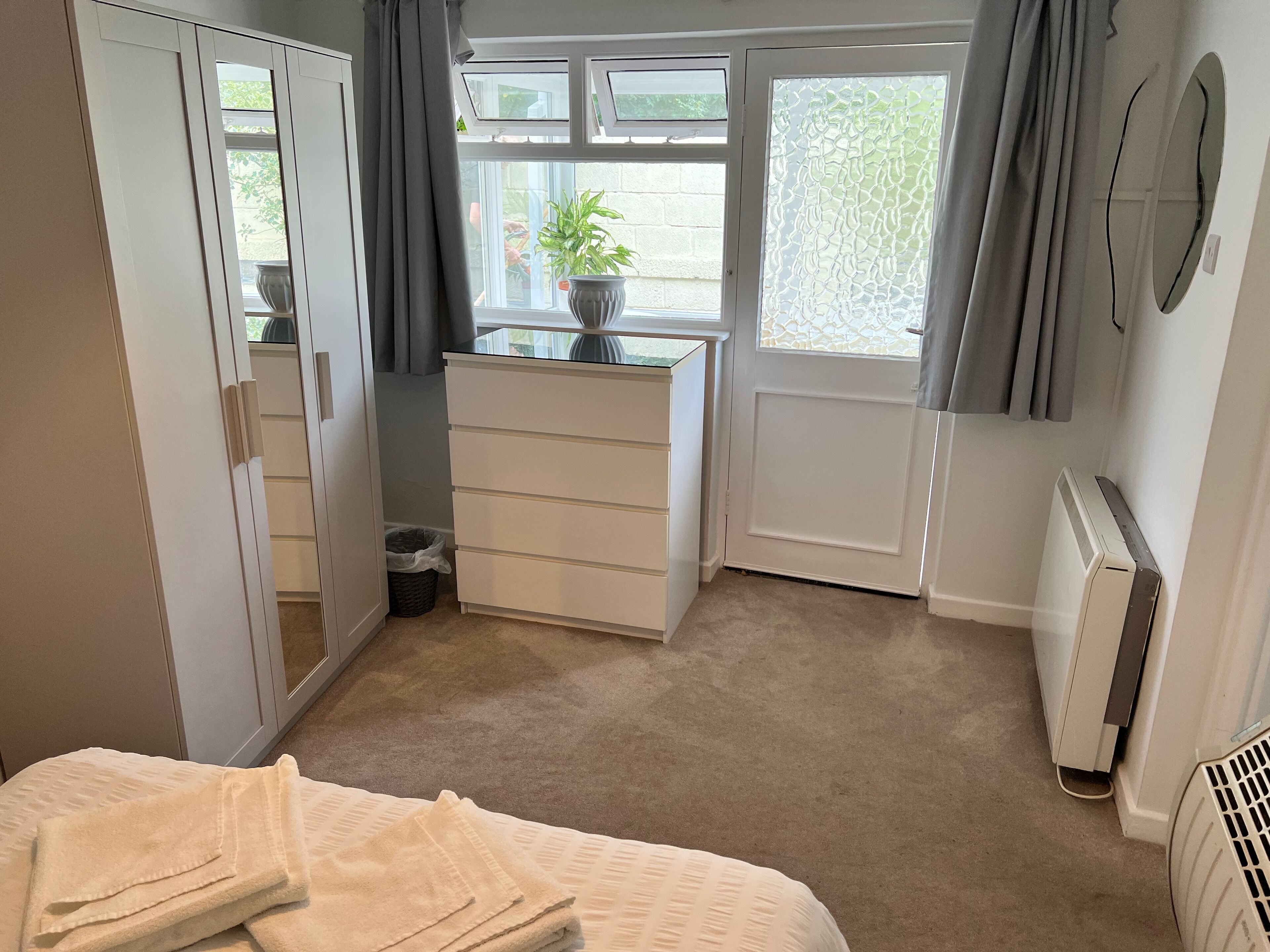 Un dormitorio con cama, cómoda, radiador y ventana con cortinas.