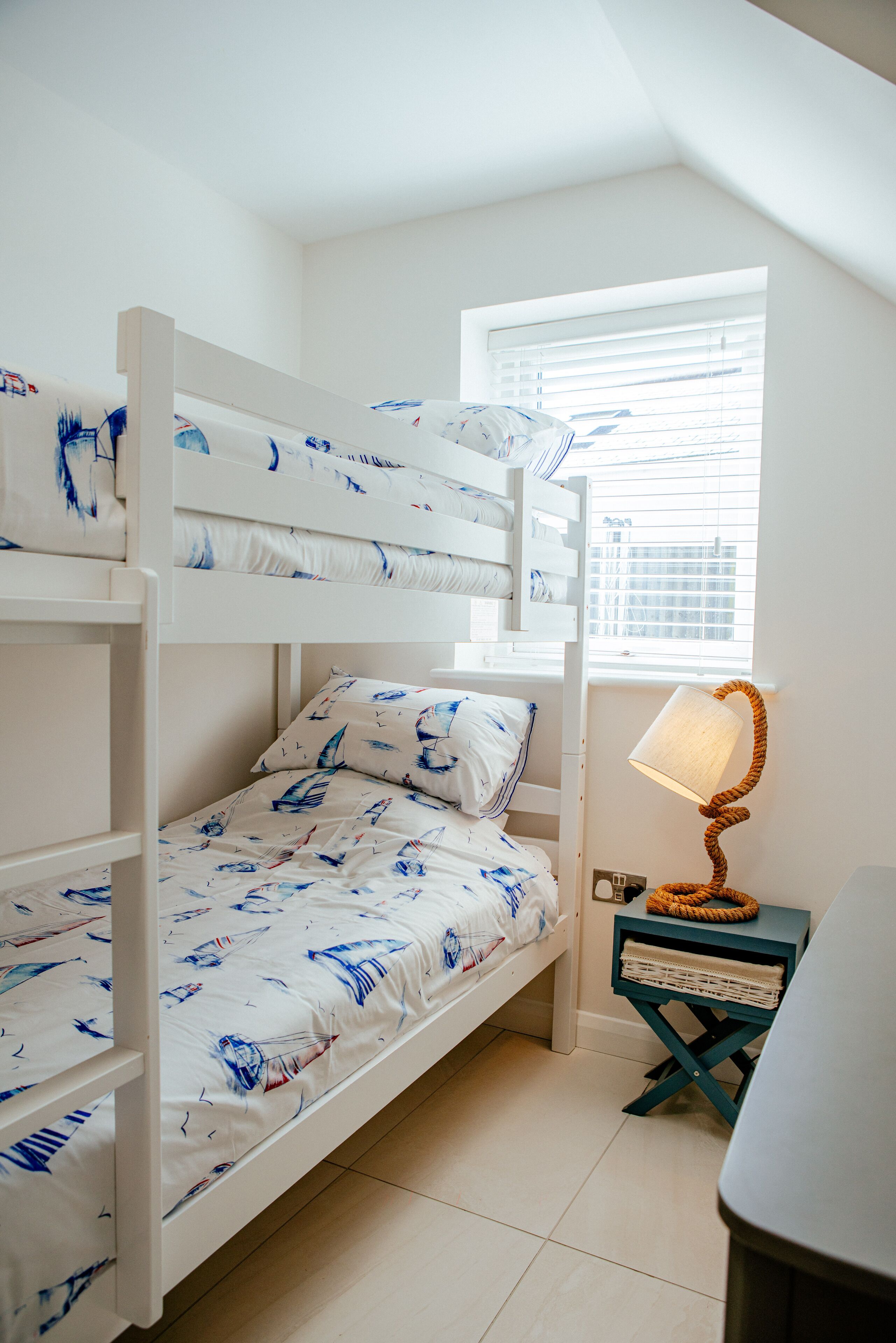 Une chambre avec un lit superposé, une fenêtre, une lampe et une petite table.