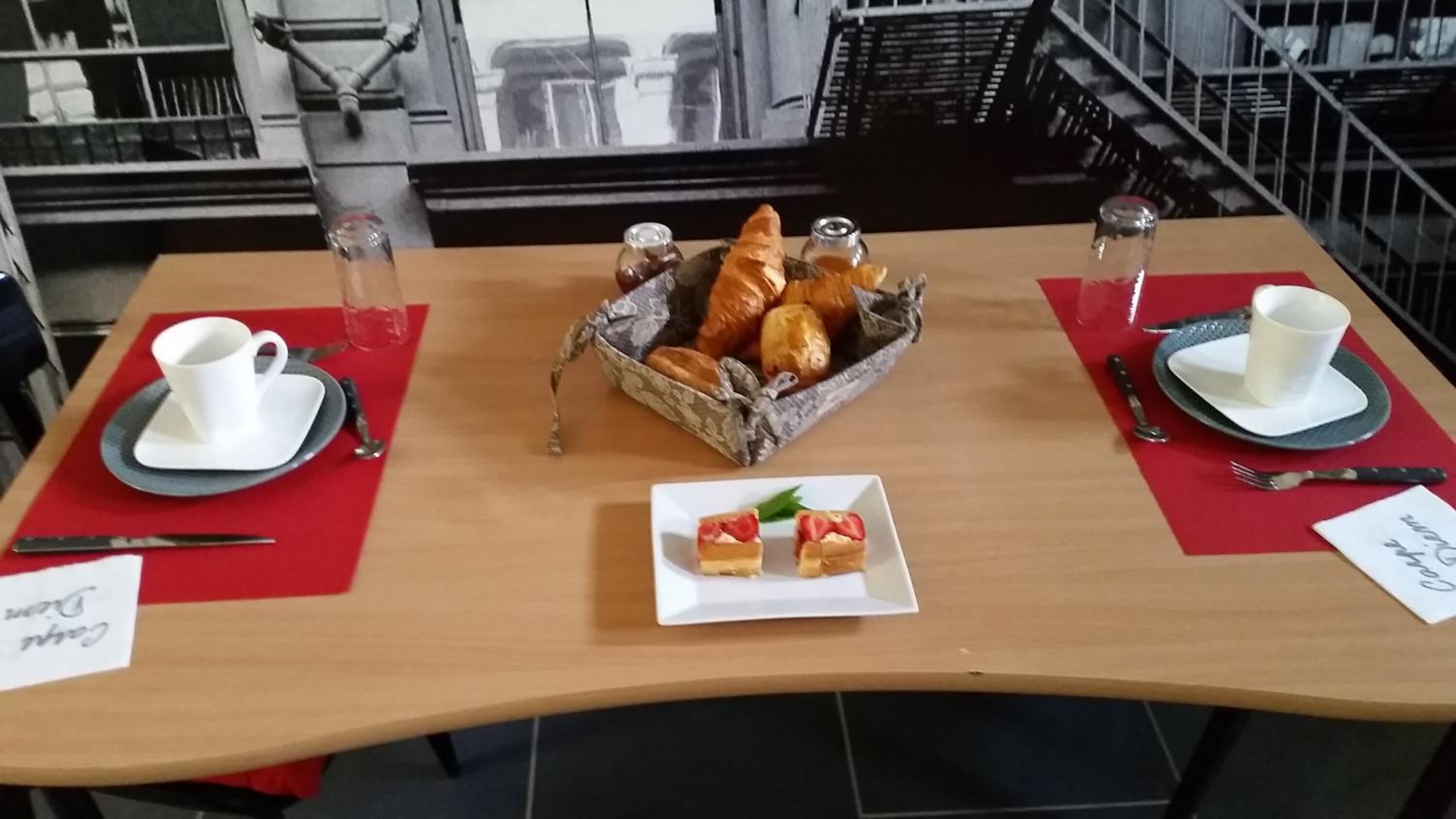 A breakfast setup with croissants, a small plate of pastries, and two cups on red placemats.
