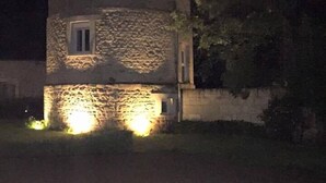 Una torre de piedra con una ventana pequeña y una puerta, iluminada por focos desde el suelo.