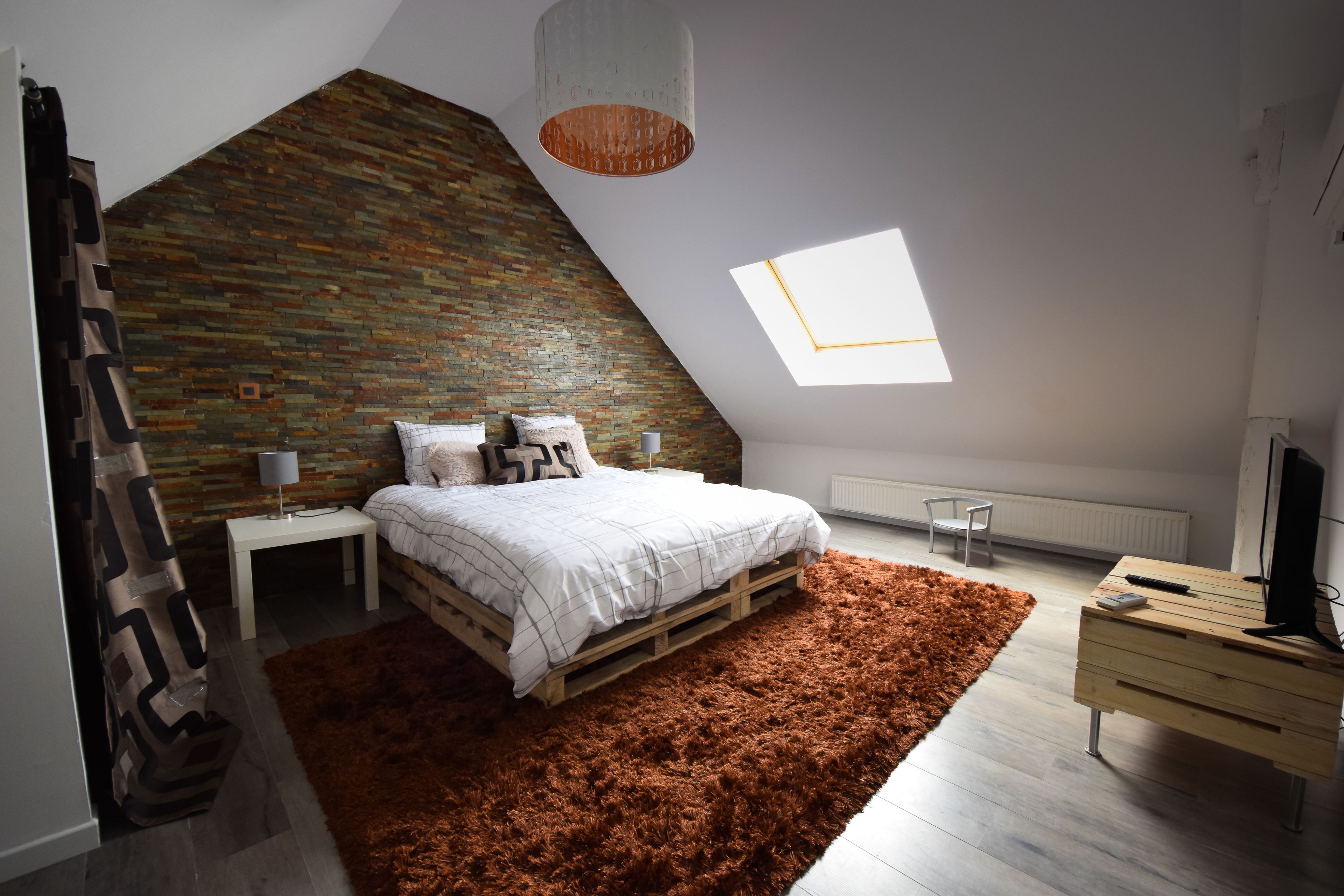 Un dormitorio con techo inclinado, una cama en camarote, una alfombra de pelo alto marrón, un aparador de madera y un televisor.