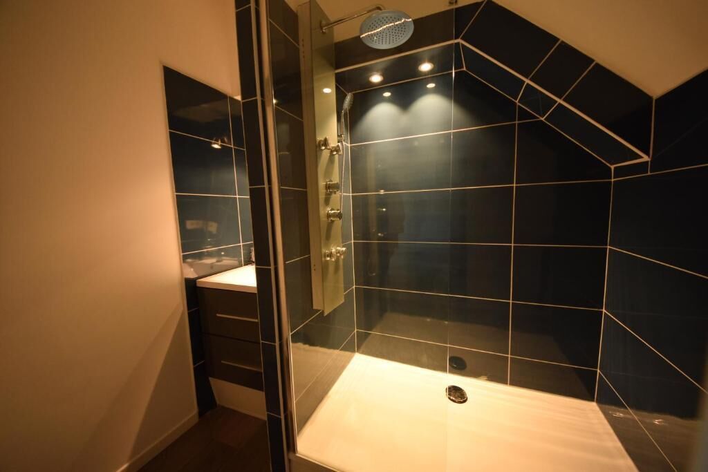 Un baño moderno con cabina de ducha de vidrio, un lavamanos blanco y paredes cubiertas de azulejos oscuros.