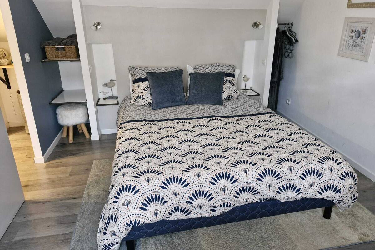 Un dormitorio con una cama grande, un taburete pequeño, un escritorio y una estantería con cestas.