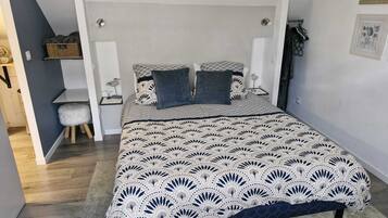 Een slaapkamer met een groot bed, een klein krukje, een bureau en een plank met manden.