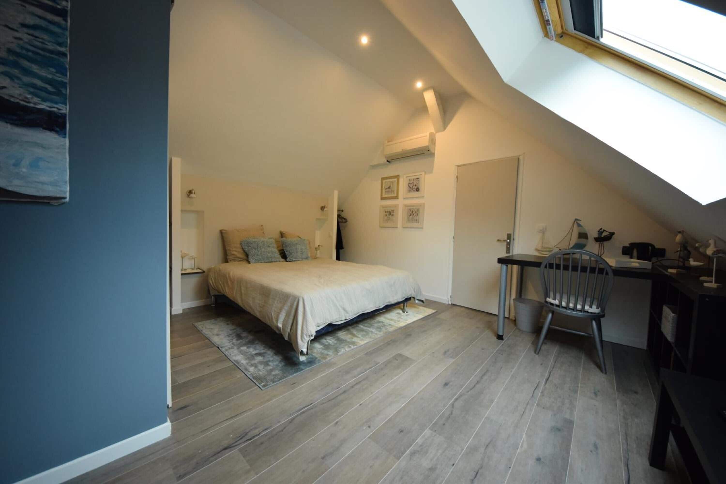 A bedroom with a bed, a desk, and a chair. There is a skylight above the bed.