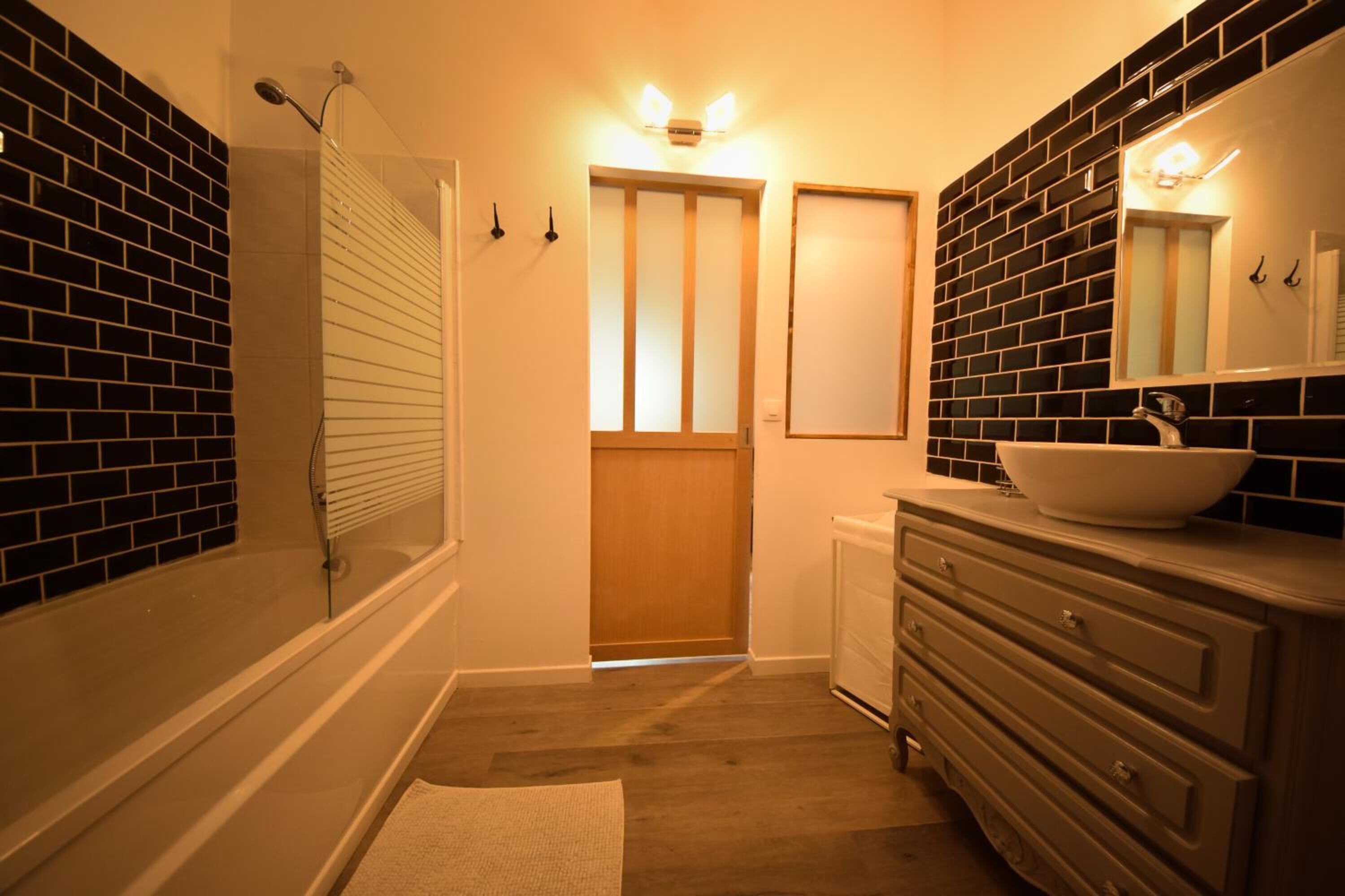 Une salle de bain avec une baignoire, un lavabo avec un miroir et une porte donnant sur une autre pièce.