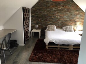Un dormitorio con techo inclinado, una cama con ropa de cama blanca, una mesita de noche pequeña, una silla y una alfombra marrón oscuro.