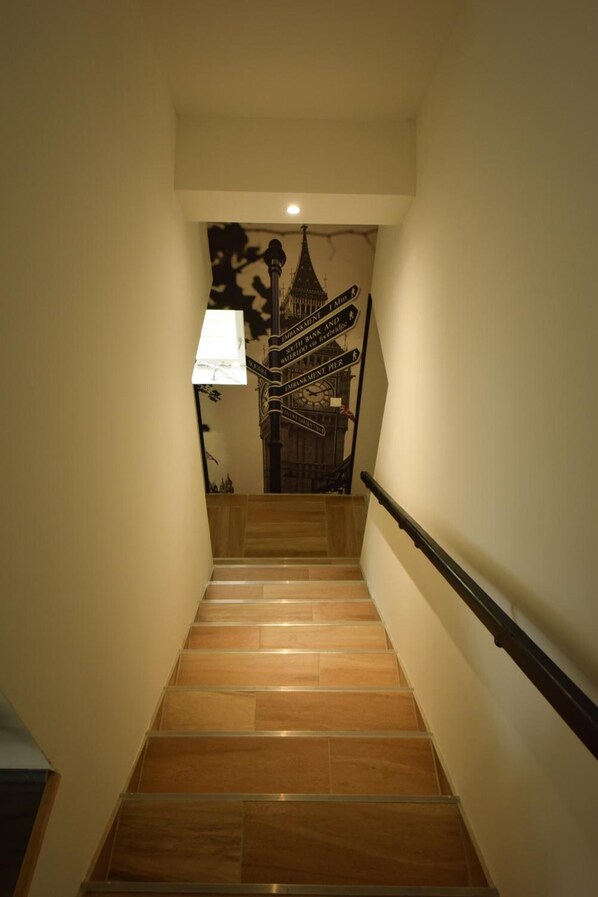 Una escalera con barandilla que lleva a una pared con un reloj y señales direccionales.