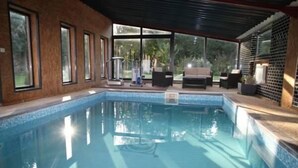 Una piscina con pared de vidrio, zona de estar techada y vista al exterior.