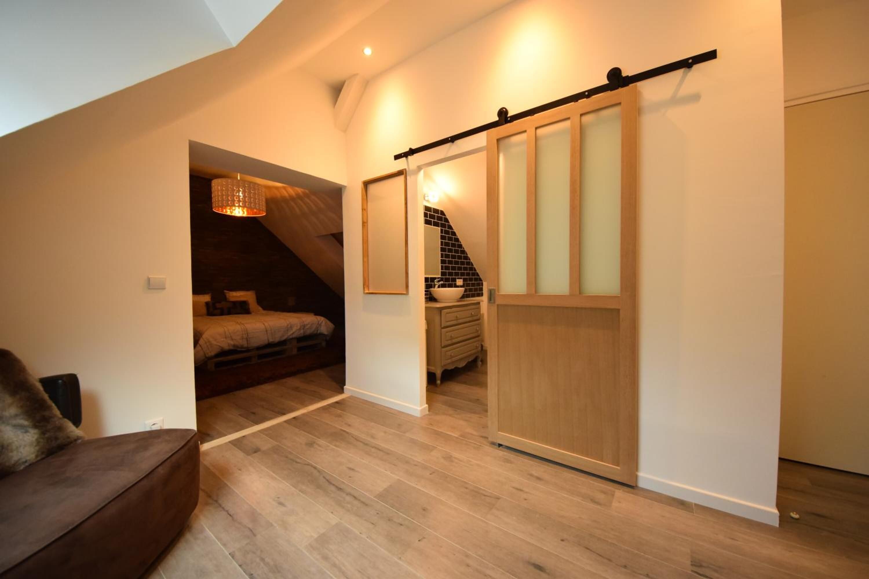A modern loft bedroom with a wooden floor, a bed, a desk, and a sliding door closet.