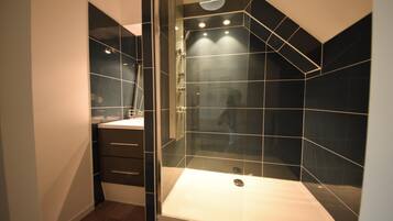 Une salle de bain moderne avec une douche à parois de verre, des murs recouverts de carreaux foncés et un lavabo blanc.