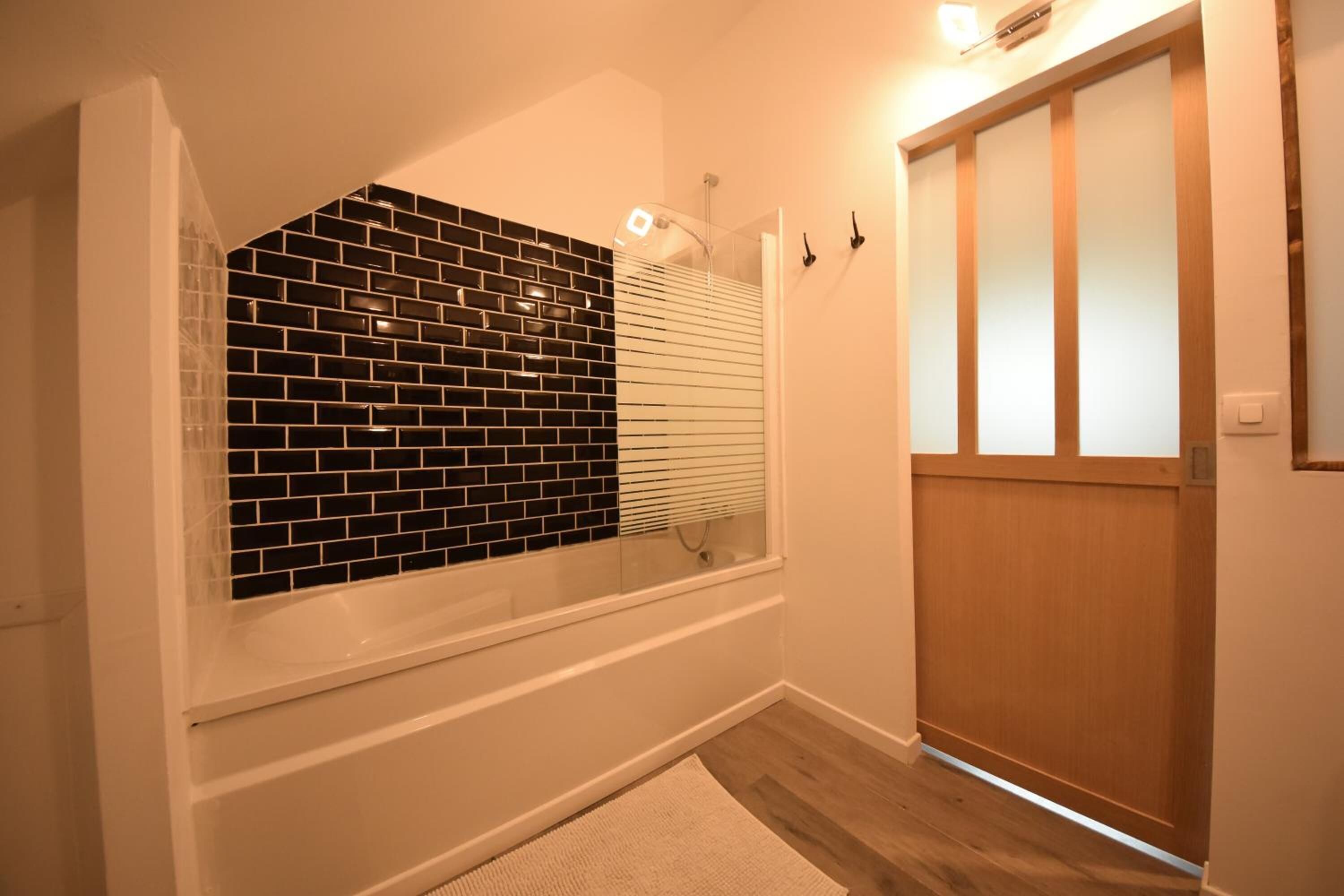 Ein Badezimmer mit Wandgestaltung aus schwarz-weißen Fliesen, einer Holztür und einer weißen Badewanne.
