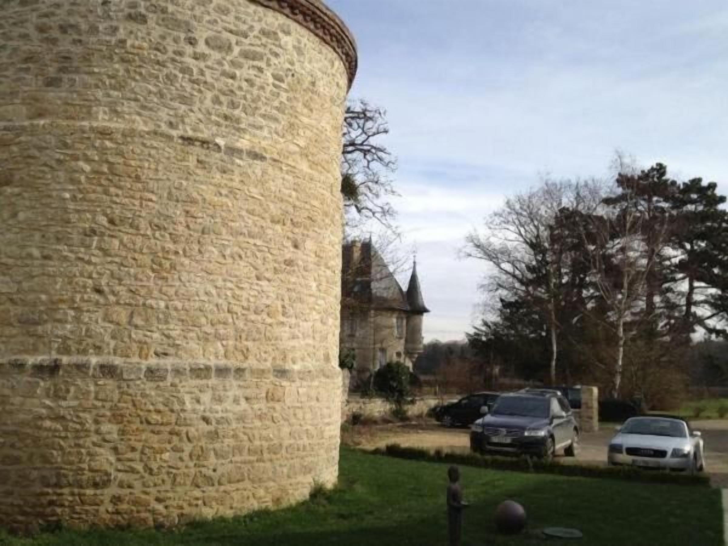 Una torre de piedra con base circular, rodeada de césped y coches aparcados.