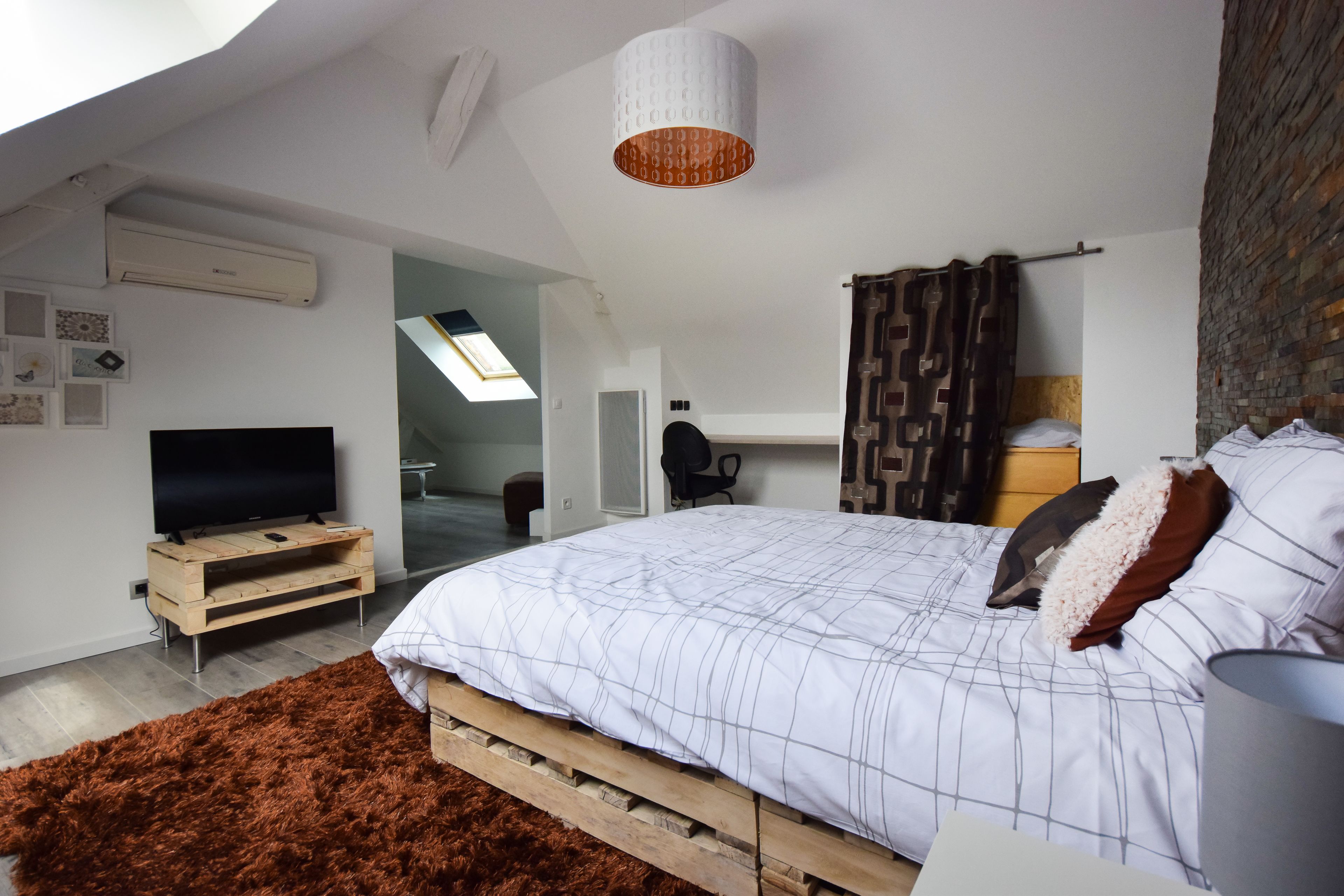 Een slaapkamer met een groot bed, een flatscreen televisie, een houten bankje en een plafondlamp.