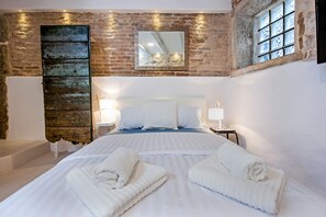 Een slaapkamer met een groot bed, twee nachtkastjes, een spiegel en een stenen muur.