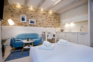 A modern room with a stone wall, a blue sofa, a bed with white linens, a small round table, and a kitchenette.