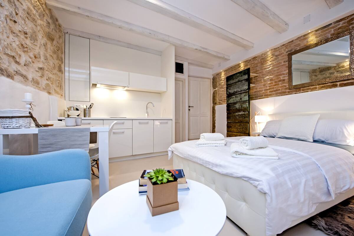 Un dormitorio moderno con una cama grande, un escritorio blanco y una pequeña zona de estar.
